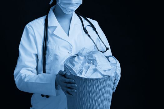 Doctor holding bucket full of used facial masks, throwing them away as symbol of epidemic ending