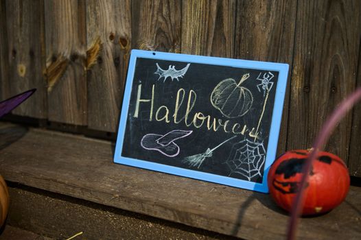A chalkboard halloween lettering on a wooden threshold and a small bright orange pumpkin. October 31. Home decoration
