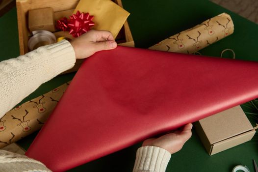 Top view crafts woman's hands, rolling out a gift paper over a surface with laid out wrapping decorative materials