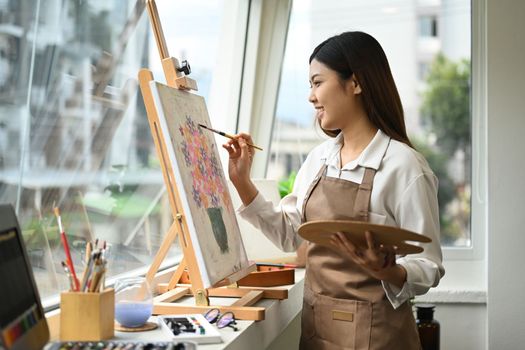 Beautiful asian woman painting picture with acrylic paints on canvas, enjoying creative leisure activities. Art and leisure activity concept