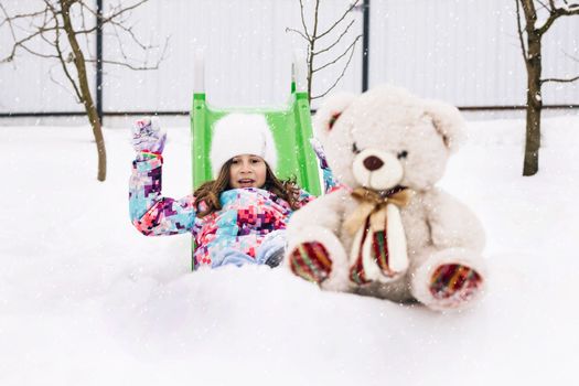 Cute toddler girl playing with teddy bear in winter park. Winter portrait of little caucasian child girl. Outdoor winter activities for kids