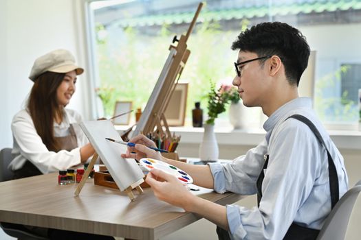 Young creative man attending in art workshop, painting picture with watercolor on canvas