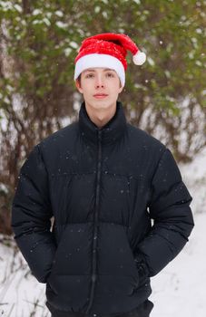 Portrait of a teenage boy in a Santa hat on a background of snowy nature.