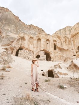 Happy young woman on background of ancient cave formations in Cappadocia, Turkey. The Monastery is one of the largest religious buildings.