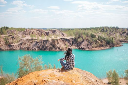 Young woman sitting on the top of mounting and feeling free and looking at the blue lake