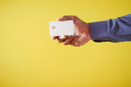 person hand holding credit card against yellow background 