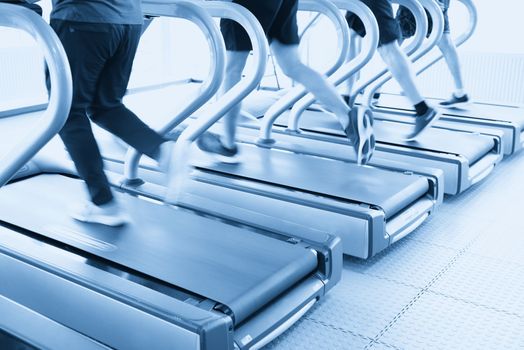 people running on machines, treadmill with motion blur, blue tone