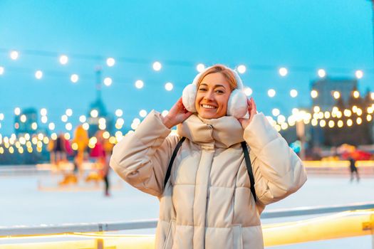 Woman winter Christmas modd Lovely middle-aged female warm winter jackets fur headphones stands ice rink background