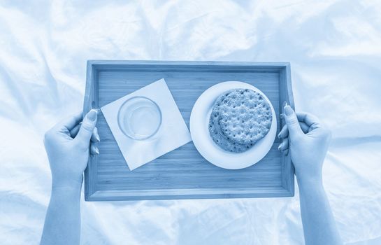 Woman holding tray with diet breakfast of crackers and water on a bed