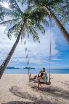 Couple on a swing on the beach with palm trees in Phuket Thailand