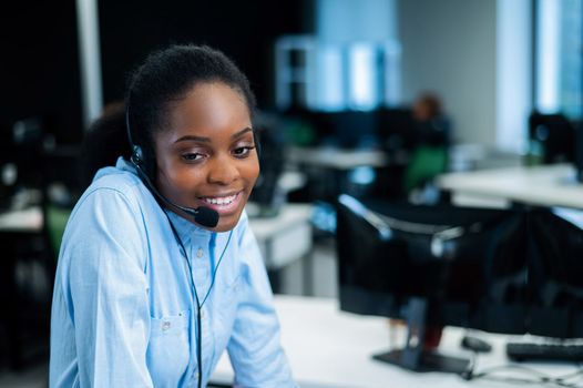 African young woman talking to a client on a headset. Female employee of the call center.