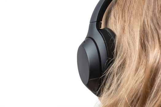 Woman in headphones isolated on white. Black headphones on a woman's head. Head of a fair-haired woman in headphones, rear view close-up.