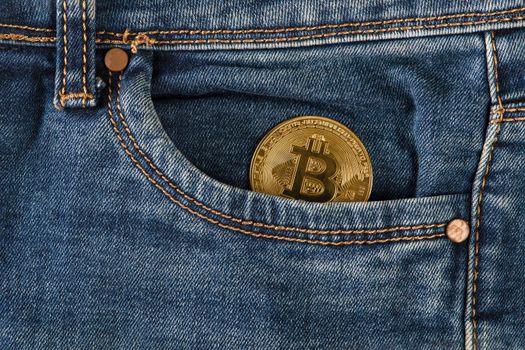 Bitcoin in your pocket. A golden bitcoin coin lies in the pocket of blue jeans. Salary in bitcoins, income in cryptocurrency.