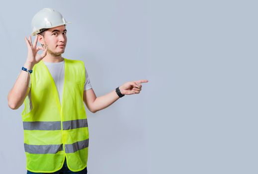 Handsome engineer recommending a product on white background, Young engineer pointing and recommending a product isolated. Builder engineer presenting a product with ok gesture