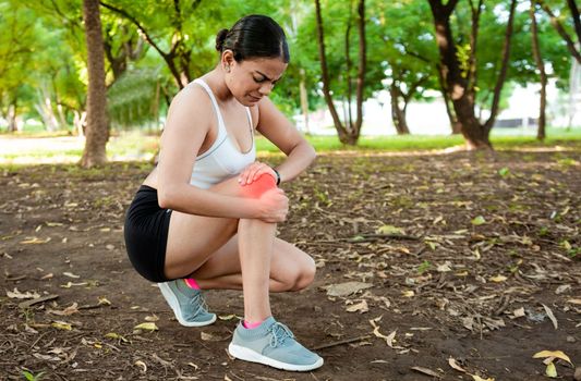 Athlete woman with knee muscle pain. Athlete girl on the ground with knee pain outdoors. Runner woman with knee pain outdoors. Athlete knee pain and fractures concept