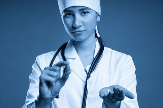 Young female doctor holding a pill, looking at it and giving it as a treatment to the patient