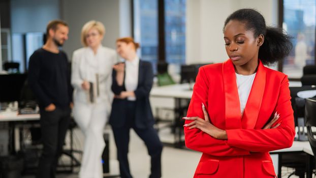 Young african woman is upset because of the ridicule of colleagues. Racial discrimination in the office.