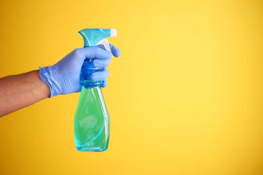 holding a plastic bottle spraying disinfect against yellow background 