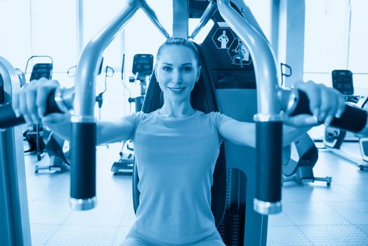 Torso portrait of Cheerful young adult caucasian woman working out on exercise machine inside gym