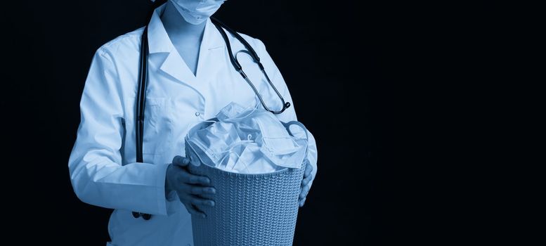Doctor holding bucket full of used facial masks, throwing them away as symbol of epidemic ending