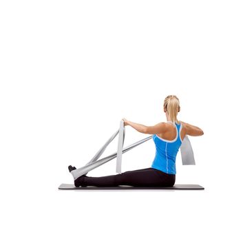 Toning with tension. A beautiful woman sitting on a mat and exercising with a resistance band.