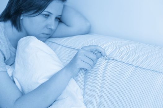 sad woman sitting on the bed holding pillow