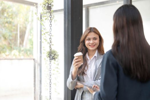 Happy two young Asian business woman holding coffee cup in coworking office