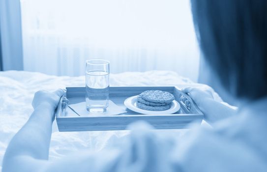 Woman holding tray with diet breakfast of crackers and water on a bed