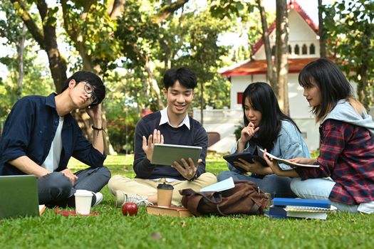 Image of university students doing group project on digital tablet while sitting in university campus. Education, Learning and community