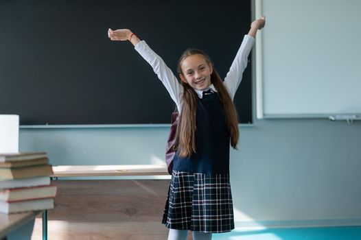 A caucasian girl stands with her arms outstretched at the blackboard. The lessons are over.