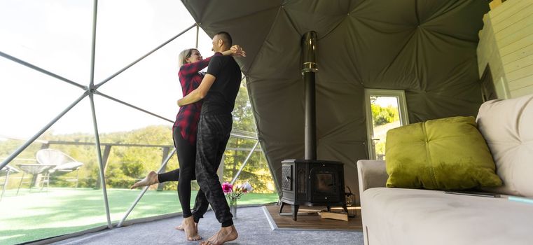 couple looking at nature from geo dome tents. Green, blue, orange background. Cozy, camping, glamping, holiday, vacation lifestyle concept. Scenic outdoors cabin