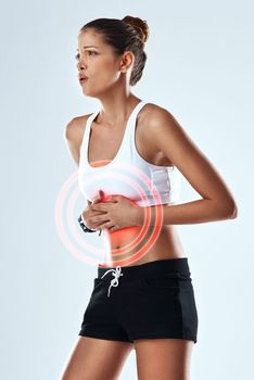 Her stomach is in knots. Studio shot of an athletic young woman holding her stomach in pain against a grey background.