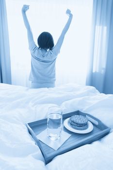 Tray with water and crackers breakfast on a bed with woman stretching on background