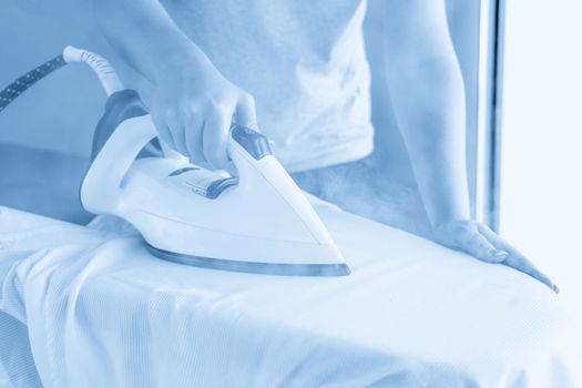 Female hands ironing white shirt on ironing board