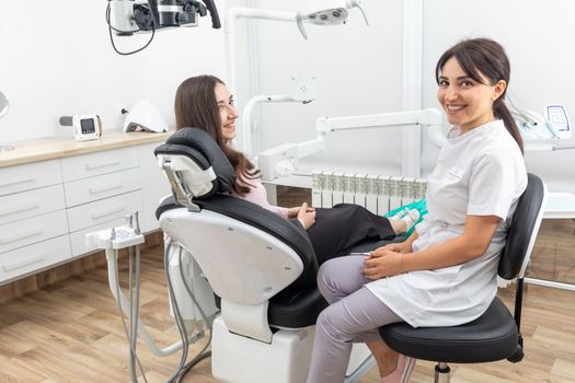 Female dentist talking to a young patient during appointment in modern dental clinic before teeth treatment