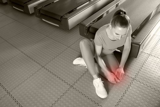 Young woman in sportswear having pain in her knee while training in gym, Girl sitting on a floor touching her knee in pain