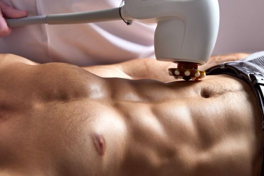 Man receiving fat reductive skin lifting body treatment on modern equipment at cosmetology clinic