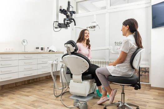Female dentist talking to a young patient during appointment in modern dental clinic before teeth treatment