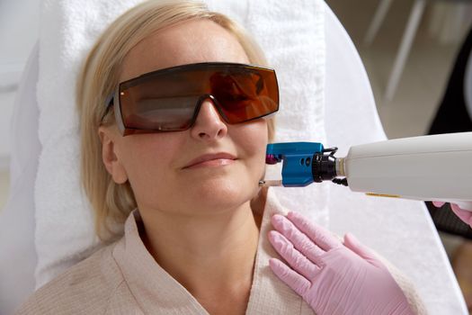 Middle aged Woman receiving laser treatment in cosmetology clinic wearing protective glasses