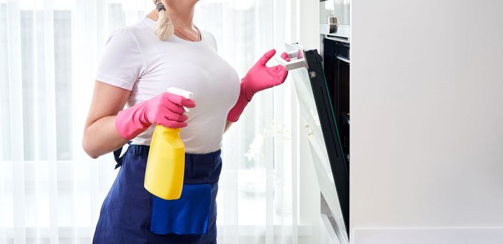 Young woman wearing gloves cleaning oven in the kitchen. Cleaning service concept