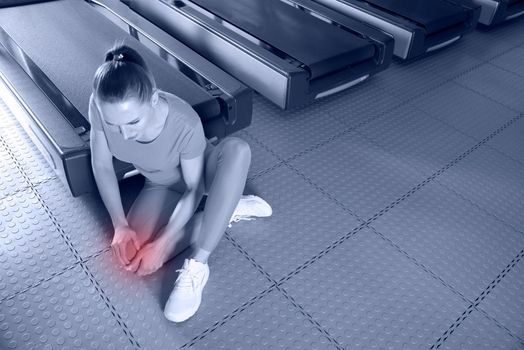 Young woman in sportswear having ache in knee while training in gym, Girl sitting on a floor touching her knee in pain