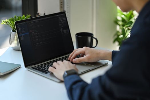 Cropped shot of IT developer typing on laptop with programming code on computer screen