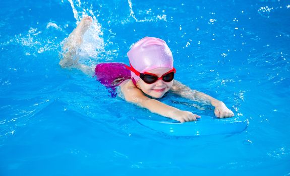 Preschool cute girl learning to swim in indoor pool with flutter board