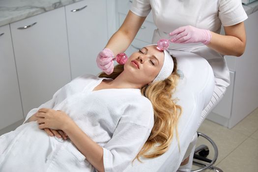 Young woman receiving facial massage with glass balls in beauty salon