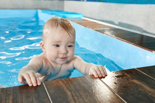 Little cute baby learning to swim in pool with trainer