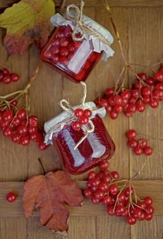 Viburnum fruit jam in a glass jar on a wooden table near the ripe red viburnum berries. Source of natural vitamins. Used in folk medicine. Autumn harvest.