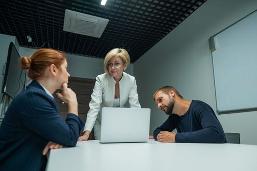 Blond, red-haired woman and bearded man in suits in the office. Business people are negotiating in the conference room.