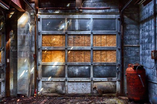 Detail of abandoned interior mechanic shop with gray garage door and red canisters