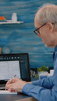 Senior man architect analysing digital prototype with plans from laptop