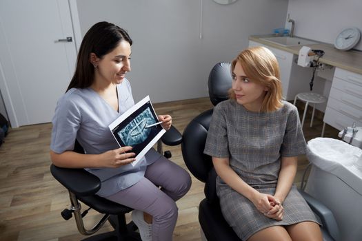 Female dentist pointing at patient's X-ray image in dental office